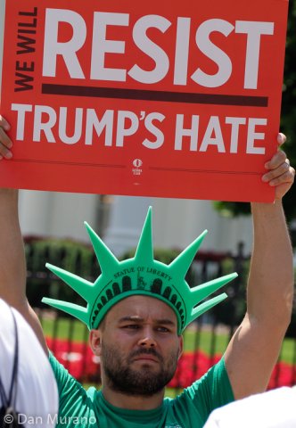 A protester holds a sign stands in front of the White House barrier.